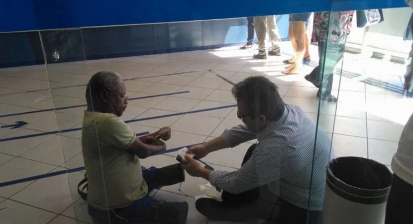 Gerente da Caixa se senta no chão para atender homem com deficiência e viraliza
